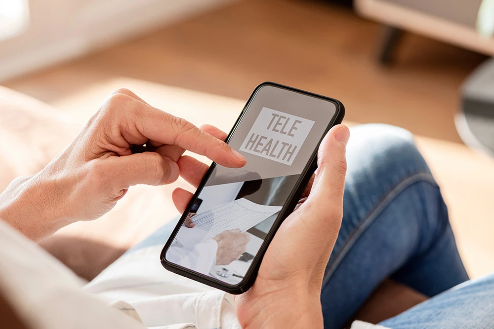 Person using a smartphone to access telehealth services, with 'Telehealth' displayed on the screen, representing remote healthcare and virtual medical consultations.